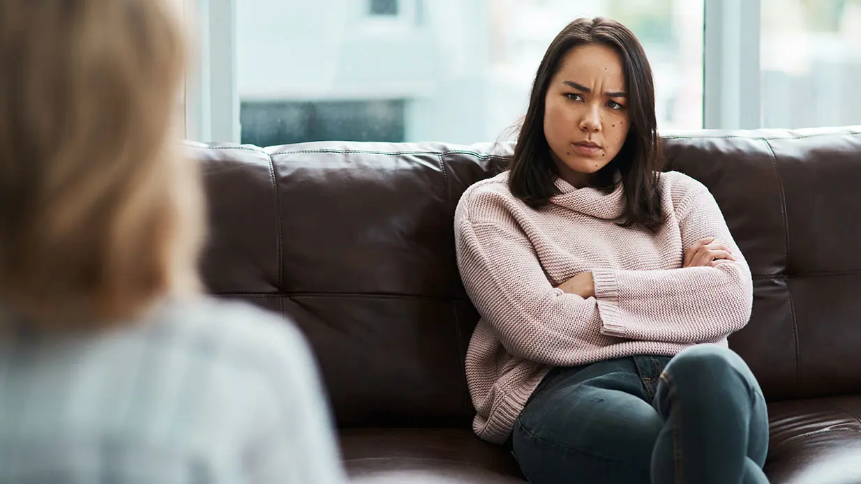 Woman sitting on a brown leather couch frowning at a person in a chair