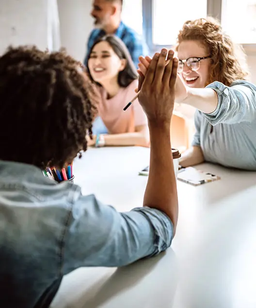 Team members high fiving over a table during a training session
