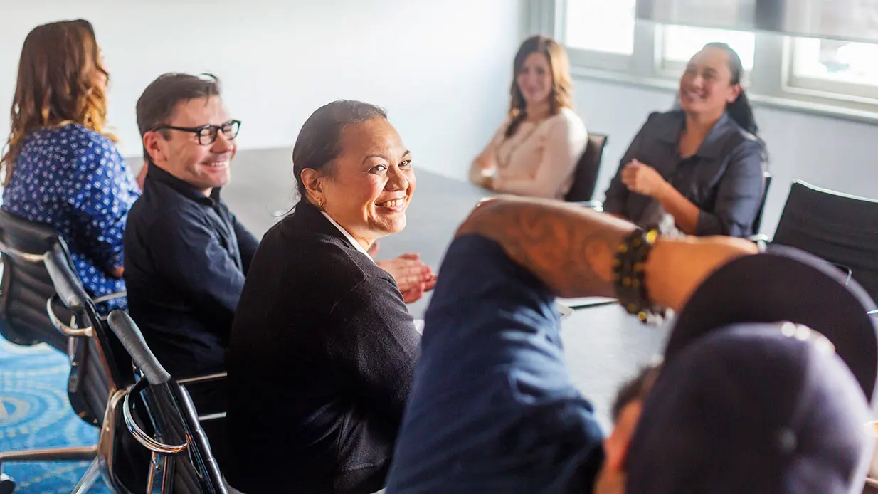 A group of people smiling at a conference room table. 
