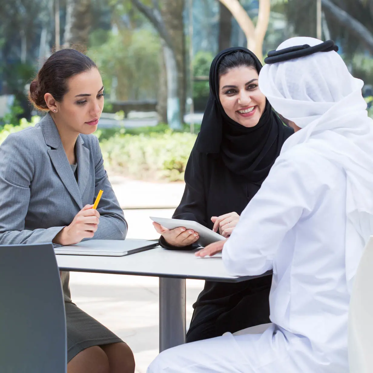 A work meeting with two women and one man taking place at a table outside. 