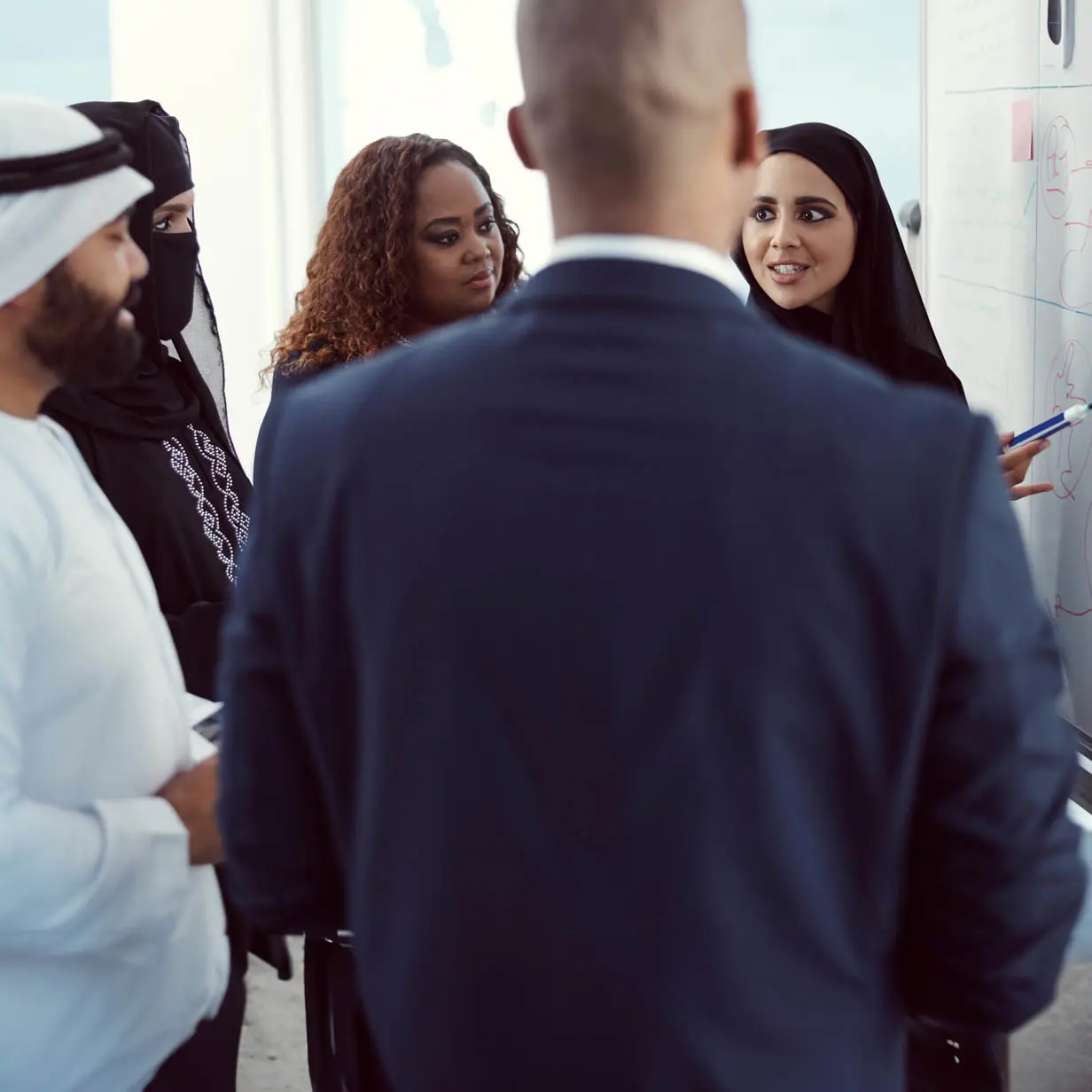 A woman speaking to a group of people and writing on a whiteboard. 