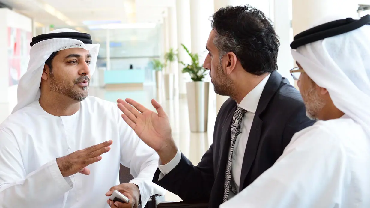 A man in a suit arguing with two men wearing keffiyehs.