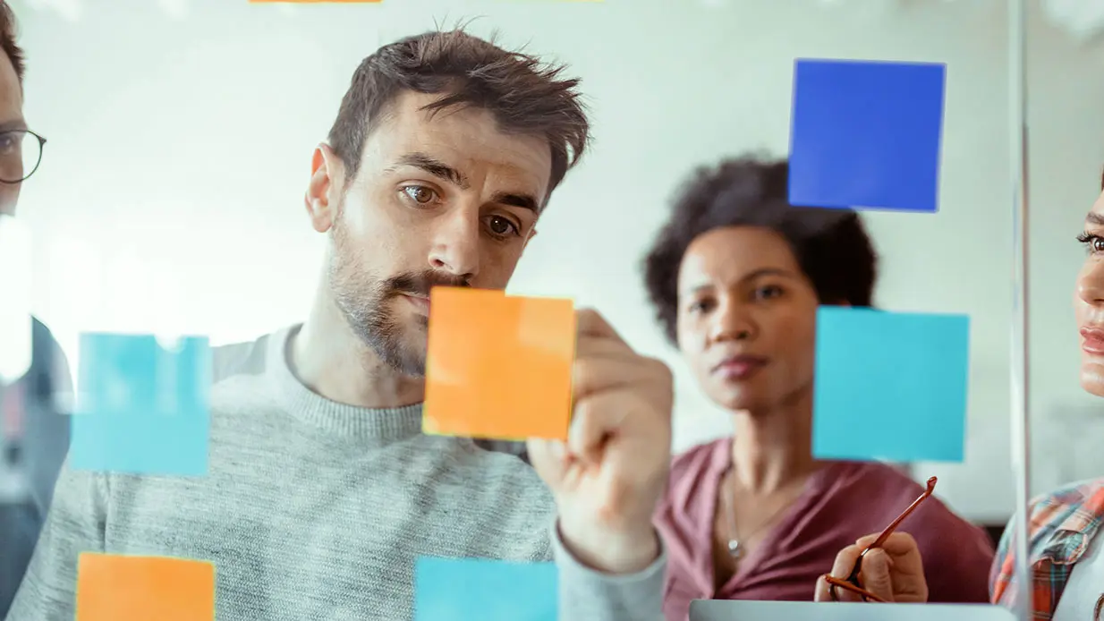 A man writing on blue and orange post-it notes during a brainstorming session.