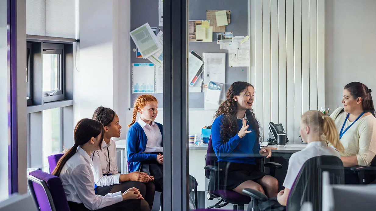 A group of students sitting down and talking to a teacher. 