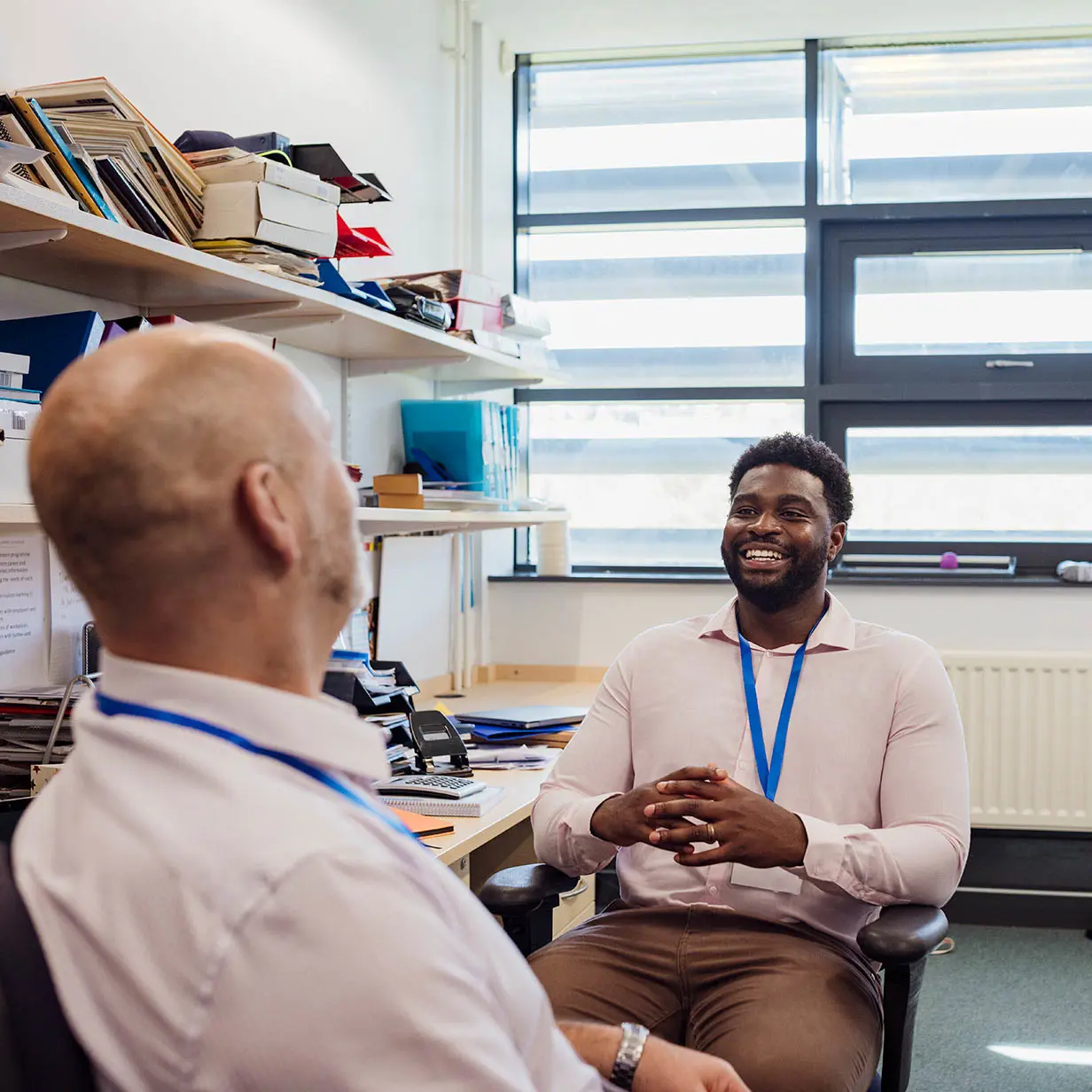 Two professionals sitting down and talking in an office. 