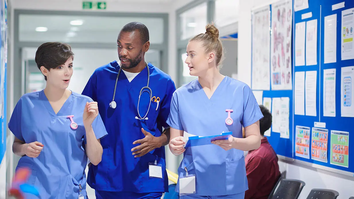 A group of three medical professionals talk as they walk down a hallway.