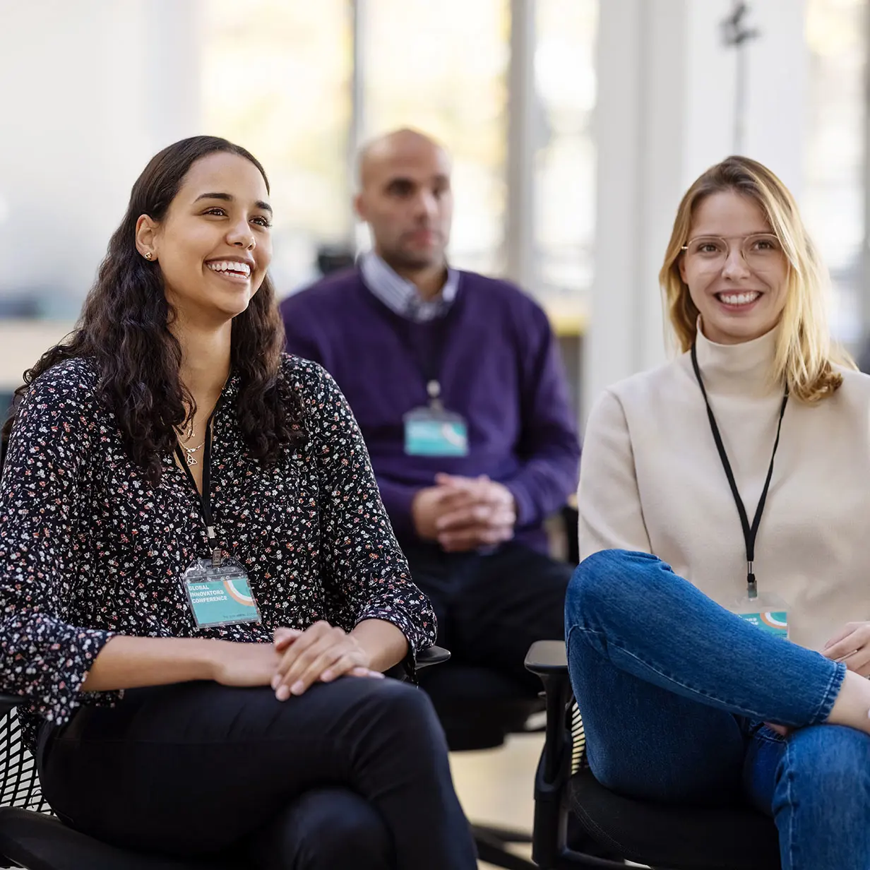 Two women sitting and smiling as they listen on. 