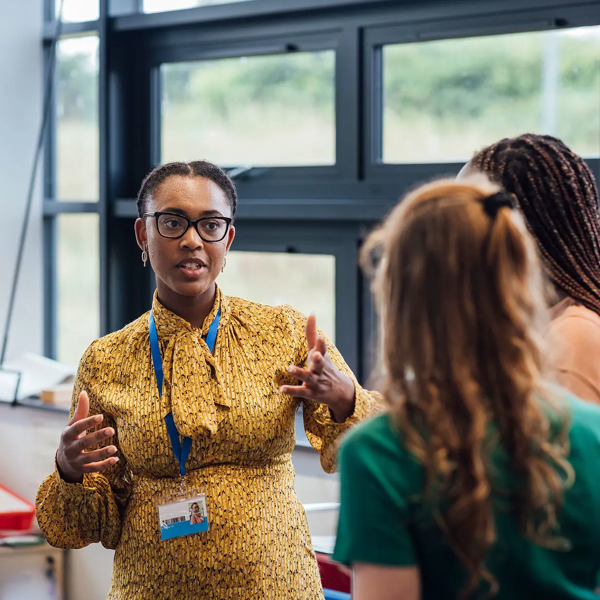 A woman in a lanyard and glasses talks with two women. 