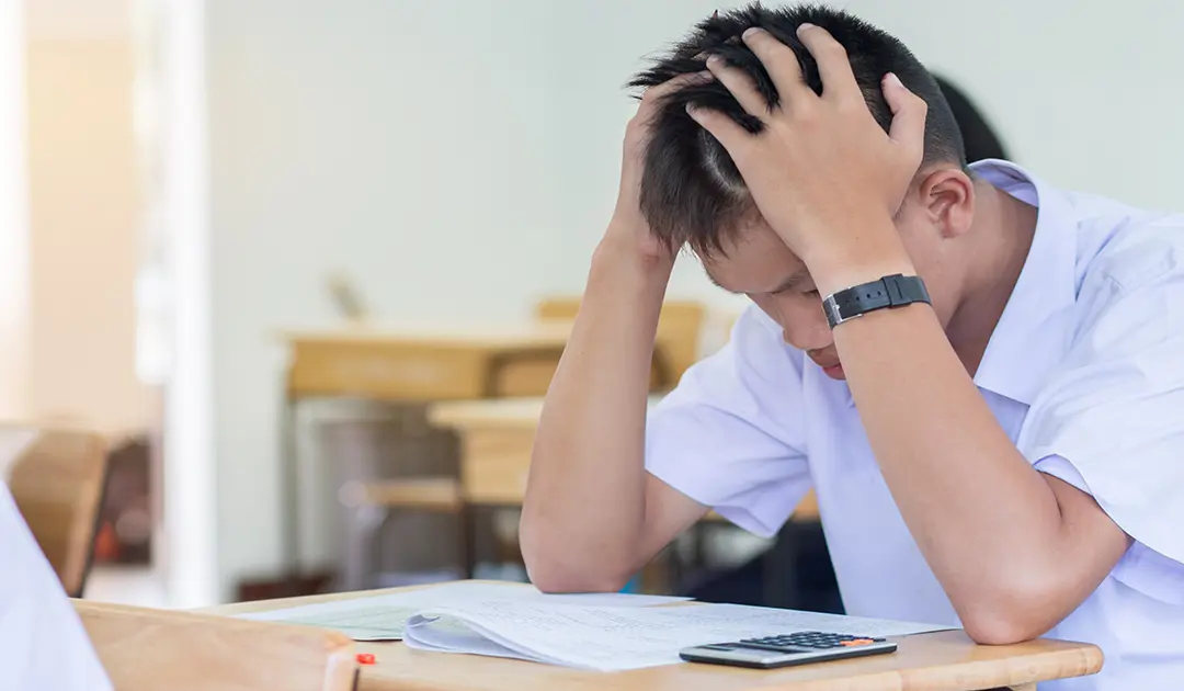 Frustrated school boy holding his head in his hands at a table
