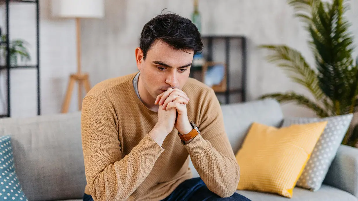 Man in tan sweater sitting on a couch thinking about Precipitating Factors
